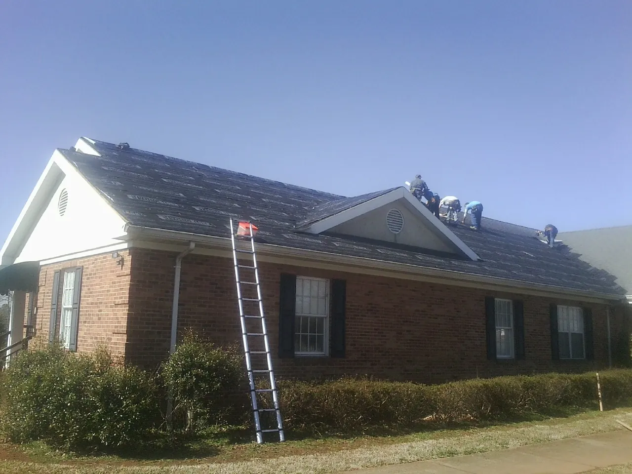 Crew tearing shingles off a brick ranch roof with a ladder set — Metal Roof Repair work by our crew in Stamping Ground