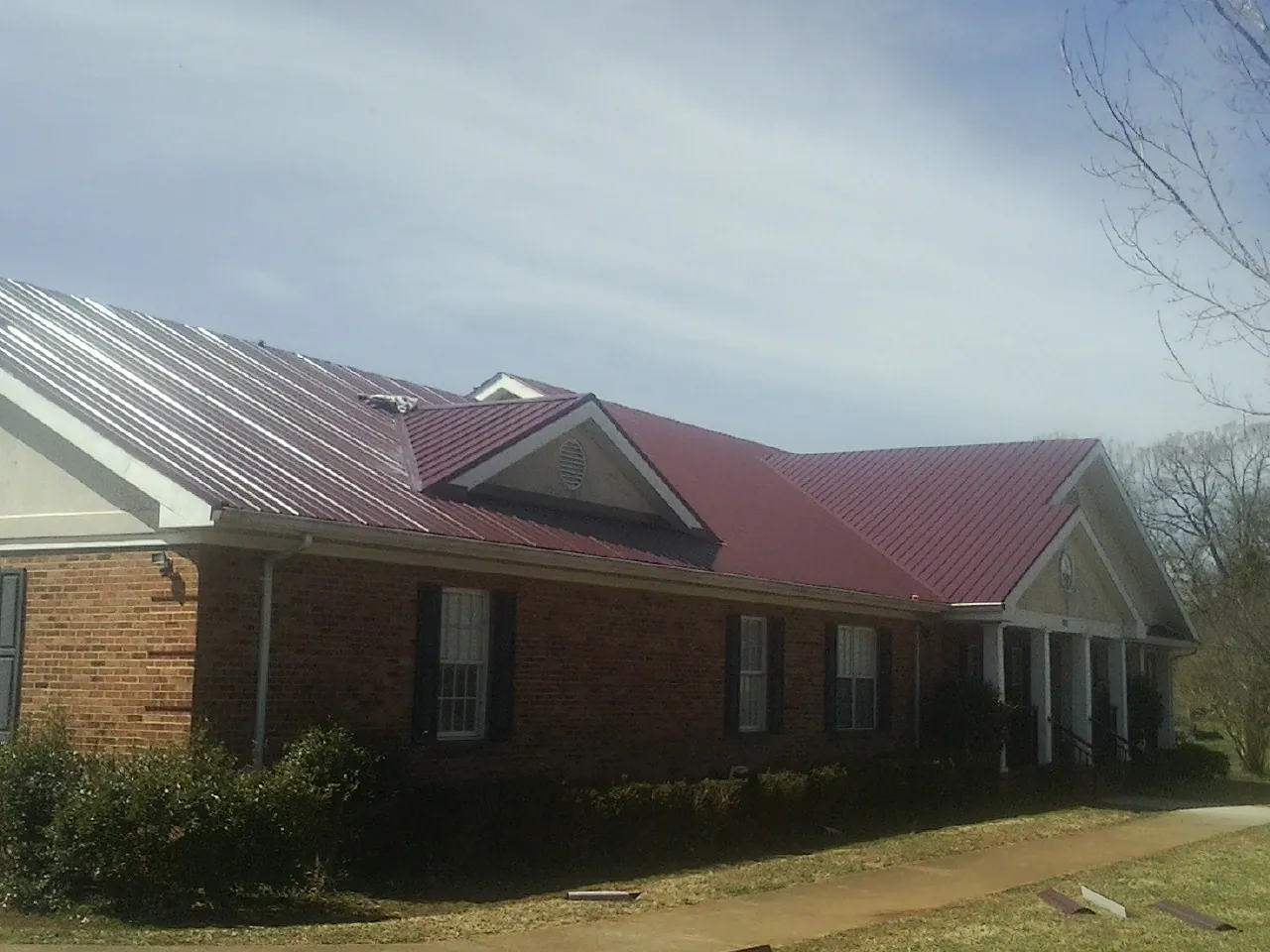 Red metal roof with gabled entries on a long brick building, from a Hail Damage Roof Repair job in Stamping Ground