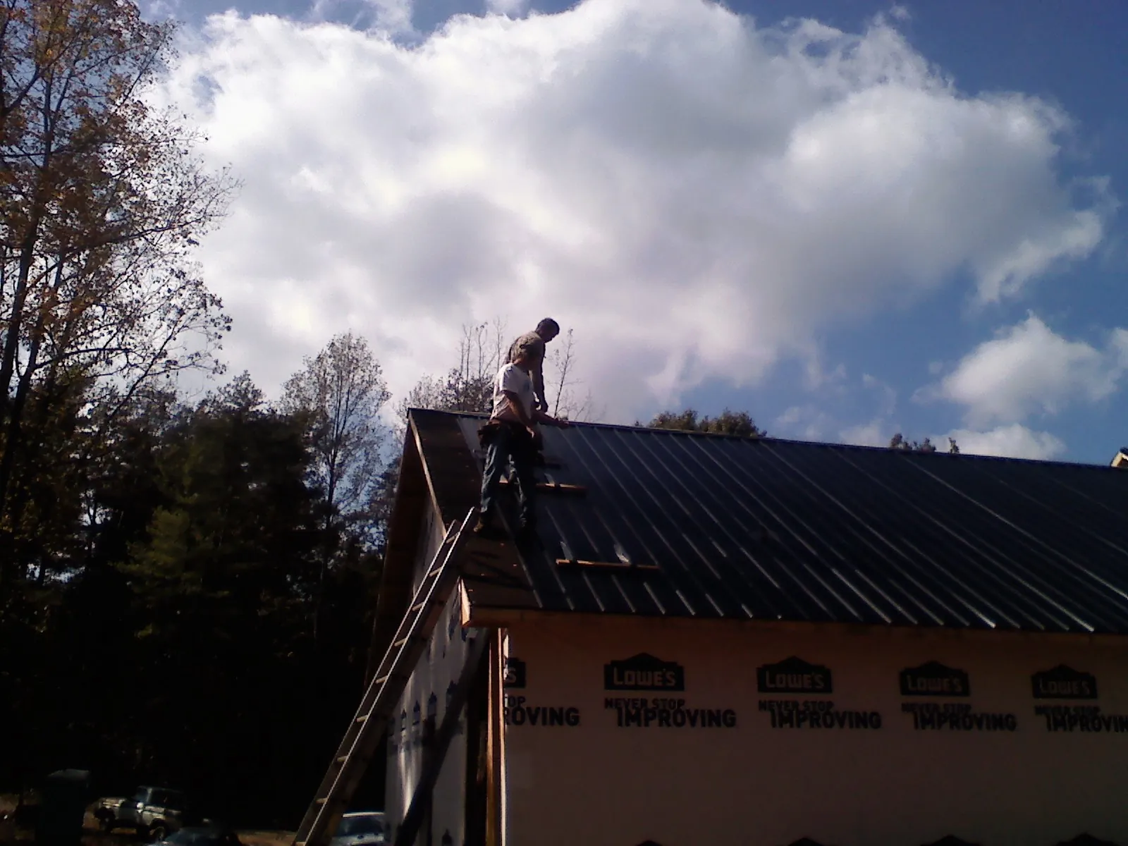 Roofer fastening dark metal panels high against a cloudy sky, from a Roof Inspection job in Stamping Ground
