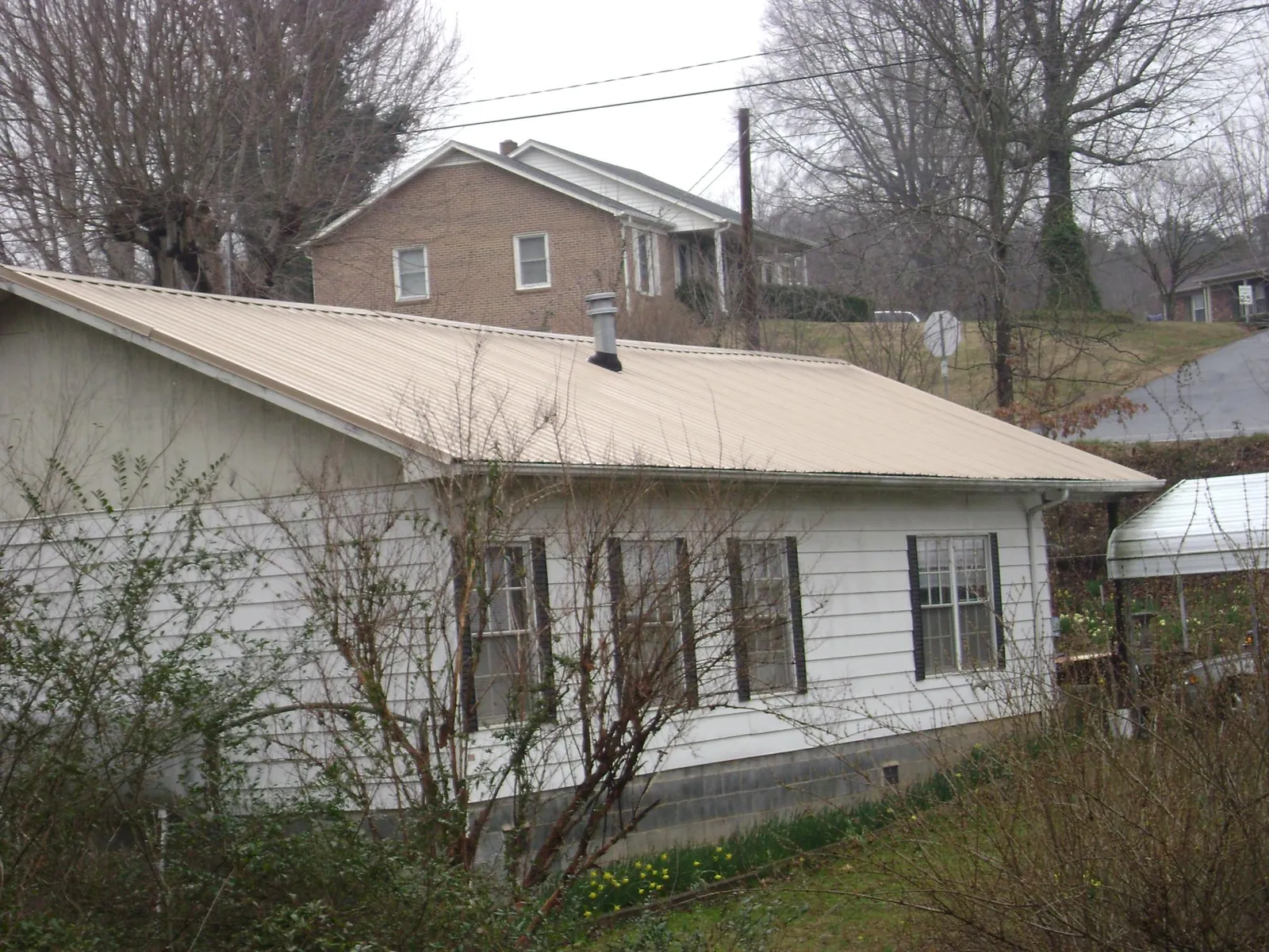 Tan metal roof on a white sided house set into a hillside — Commercial Roofing by Roofing Brothers in Stamping Ground